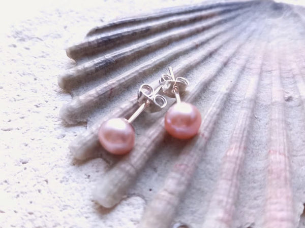 Pink pearl earrings on a shell
