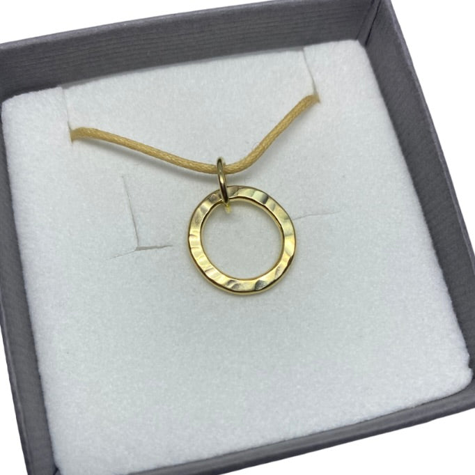 Hand textured yellow gold circle pendant displayed on a cotton thong in a gift bx