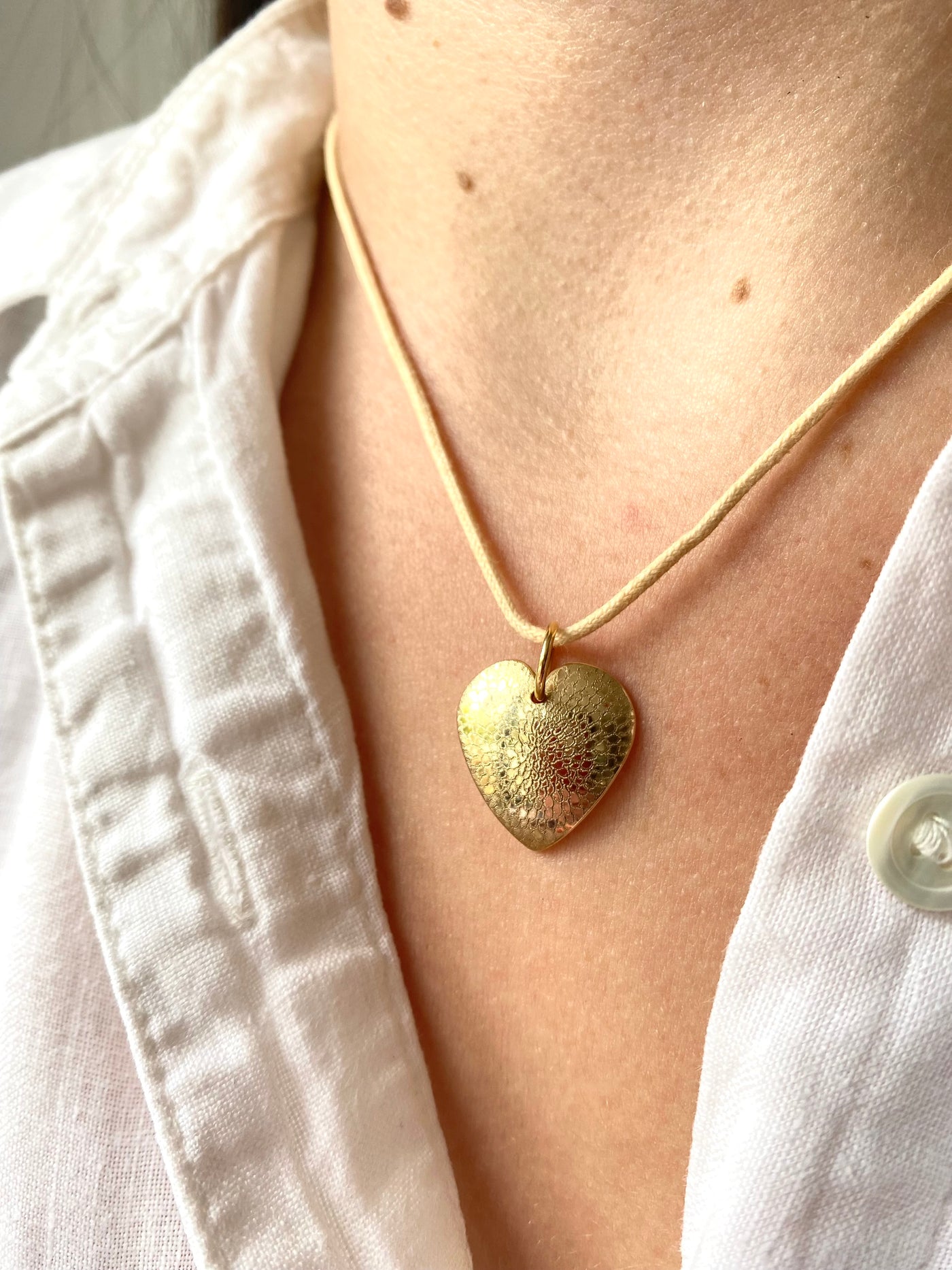 Gold heart-shaped engraved necklace with a detailed chrysanthemum design on a person wearing a white shirt.