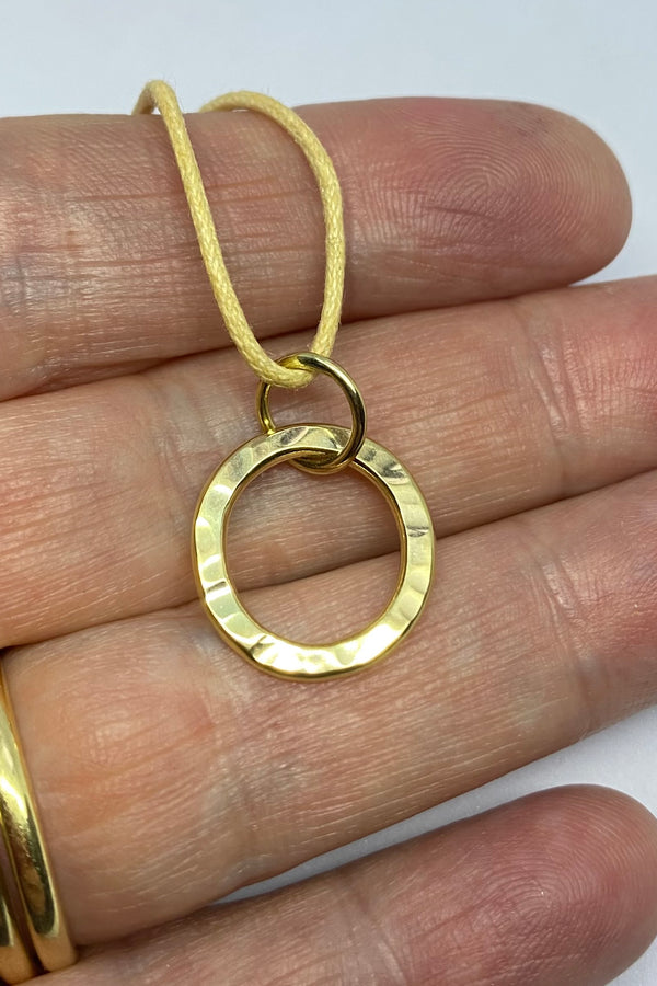 Yellow gold circle pendant with a extured surface, held on the hand that made it. 