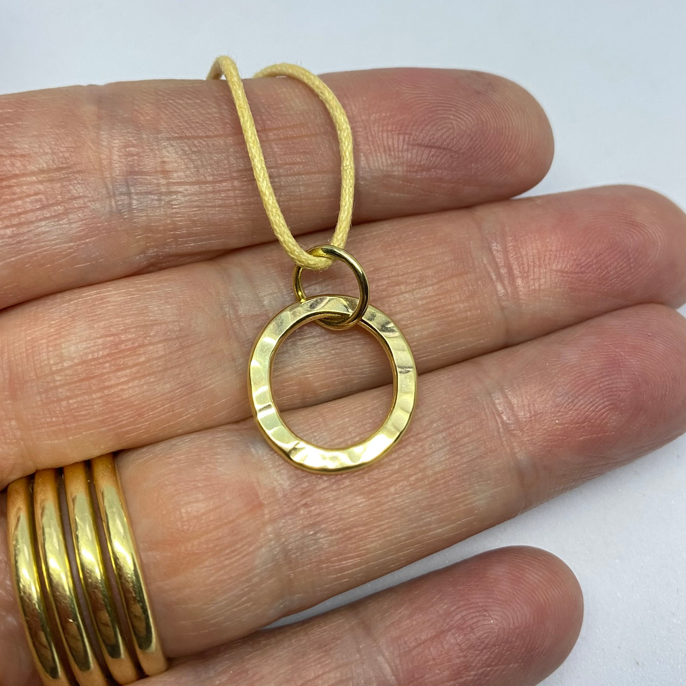 Yellow gold circle pendant with a extured surface, held on the hand that made it. 