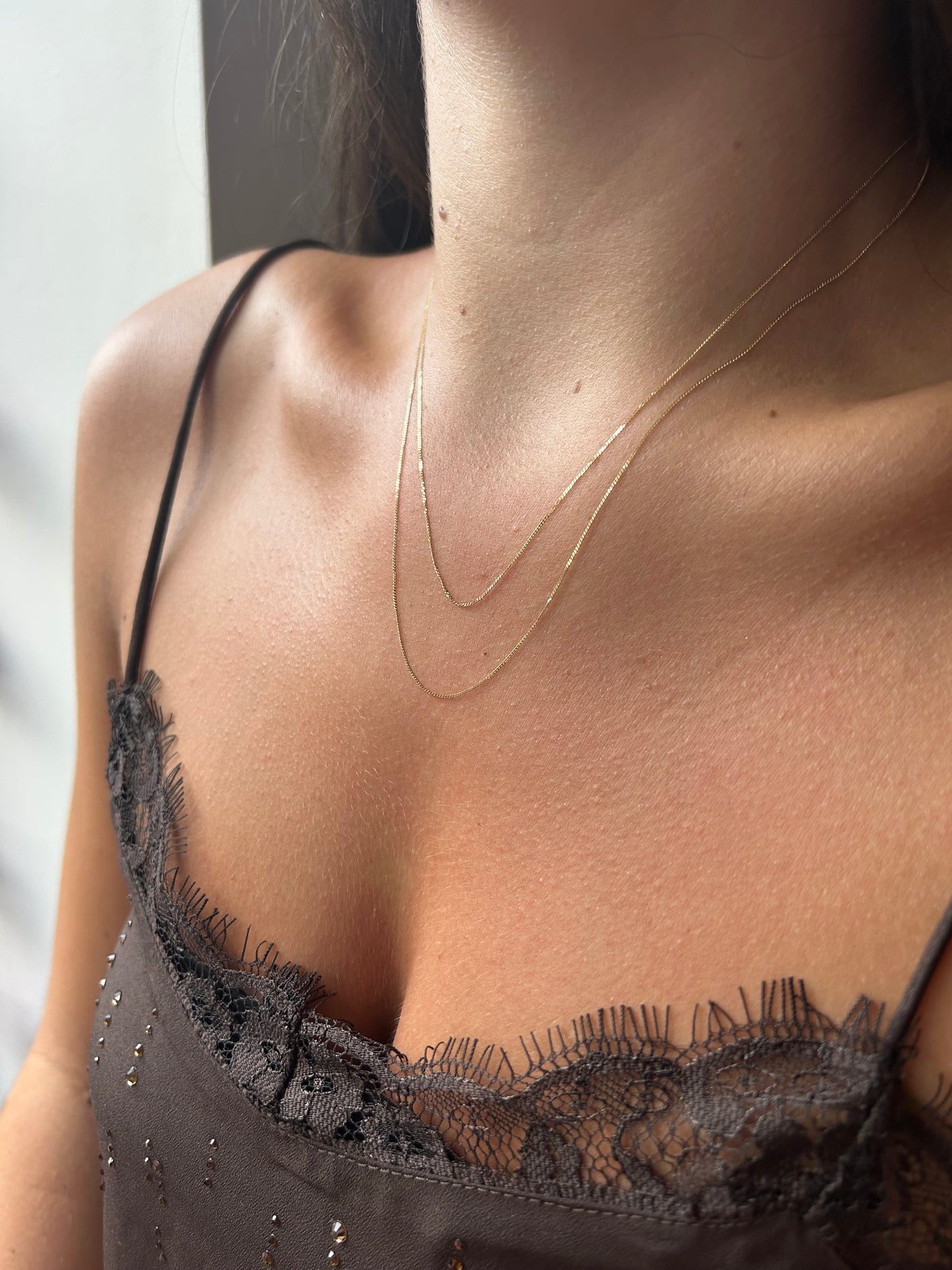Close up of a model wearing two lengths of fine gold chain to illustrate how the lengths will st on the body. 