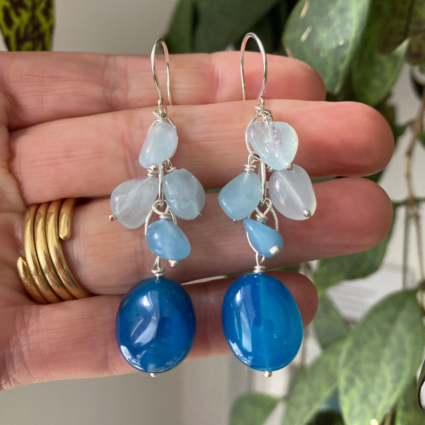 Chalcedony and aquamarine gemstone waterfall earrings in shades of dark and light blue, held by the hand that made them. 