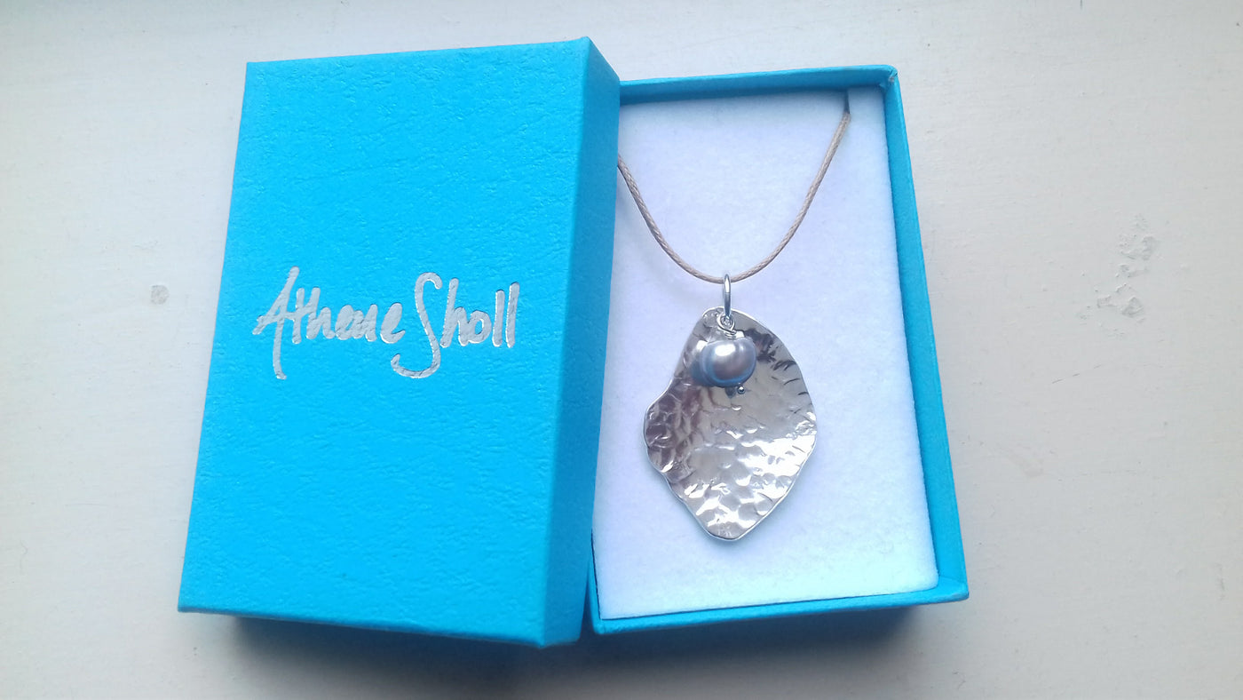 Silver potato peel textured necklace with a pendant in an open blue box with 'Athene Sholl' branding.
