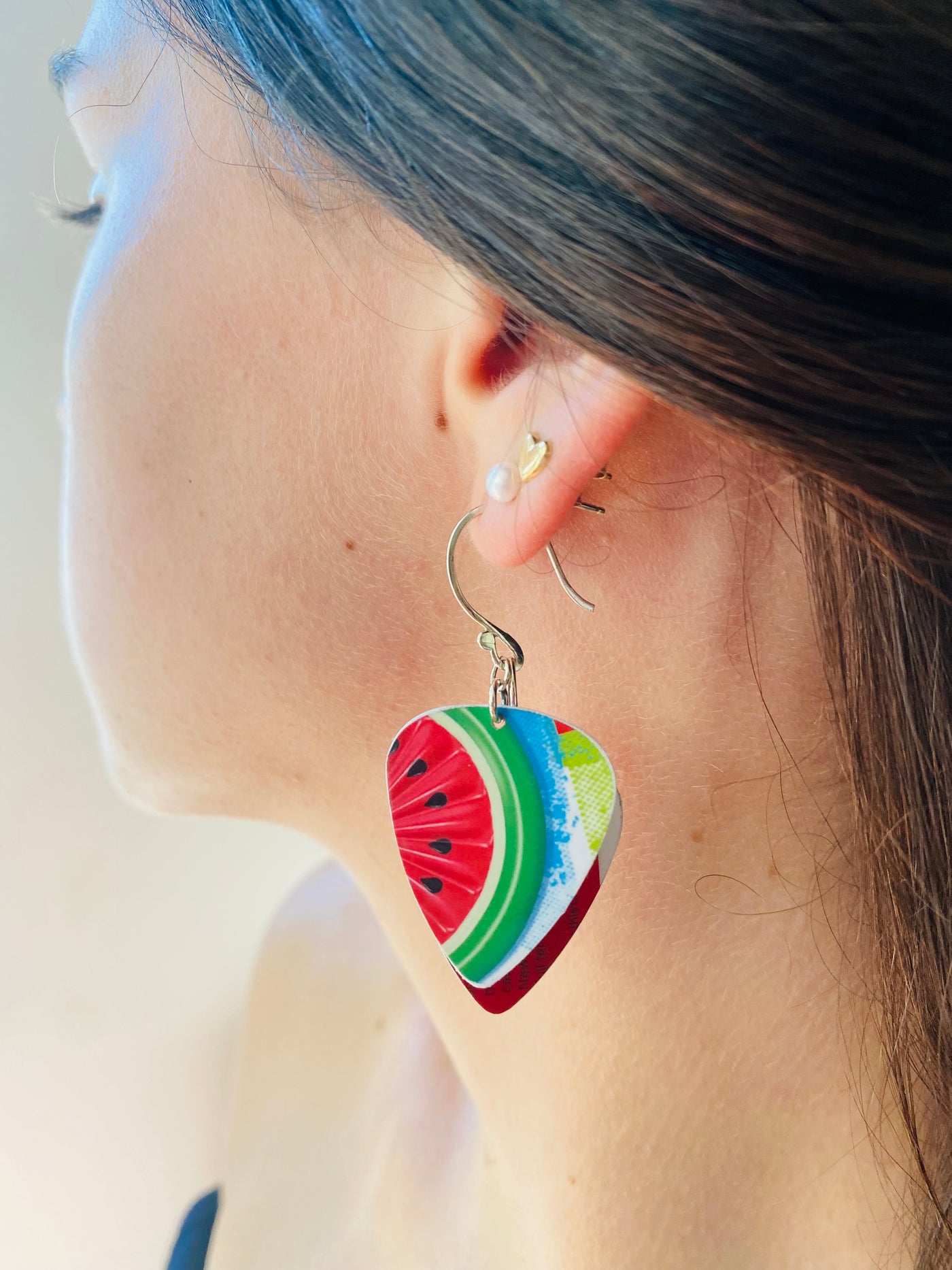 Close-up of a person wearing colorful watermelon slice earrings.