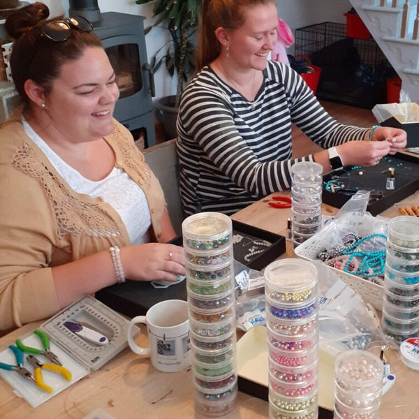 A table covered in jewellery making equipment, with two ladies making bracelets