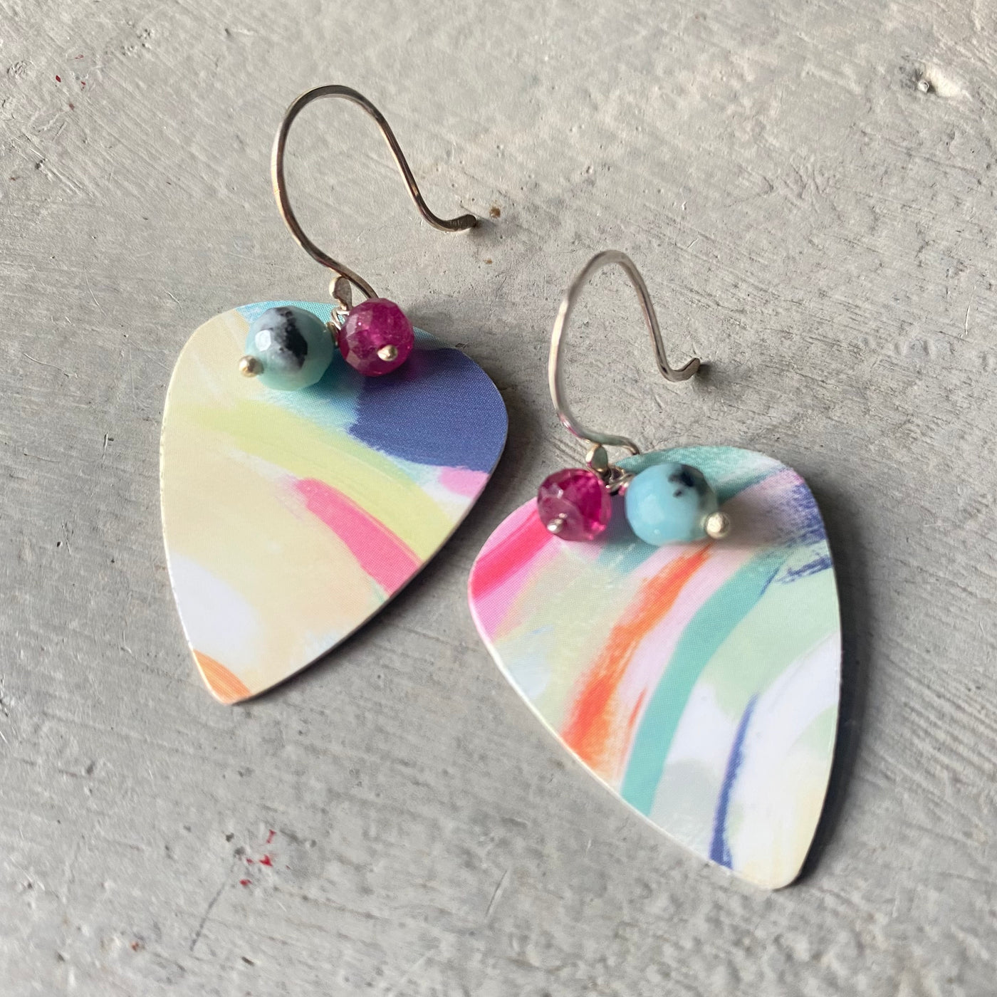 Heart-shaped earrings with colorful marbled design and pink ruby and blue amazonite beads on a gray surface