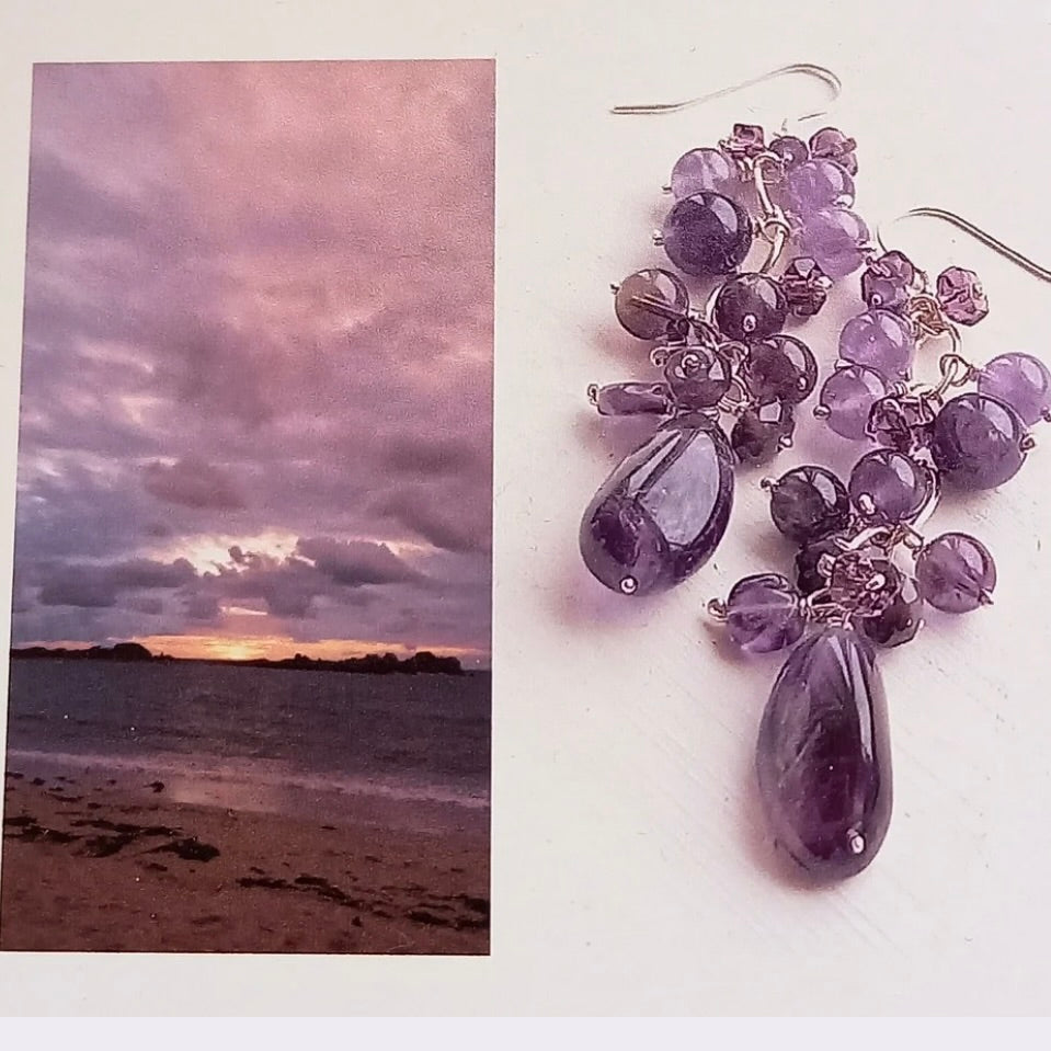 Purple beaded earrings on a white surface with the beach scene that inspired them