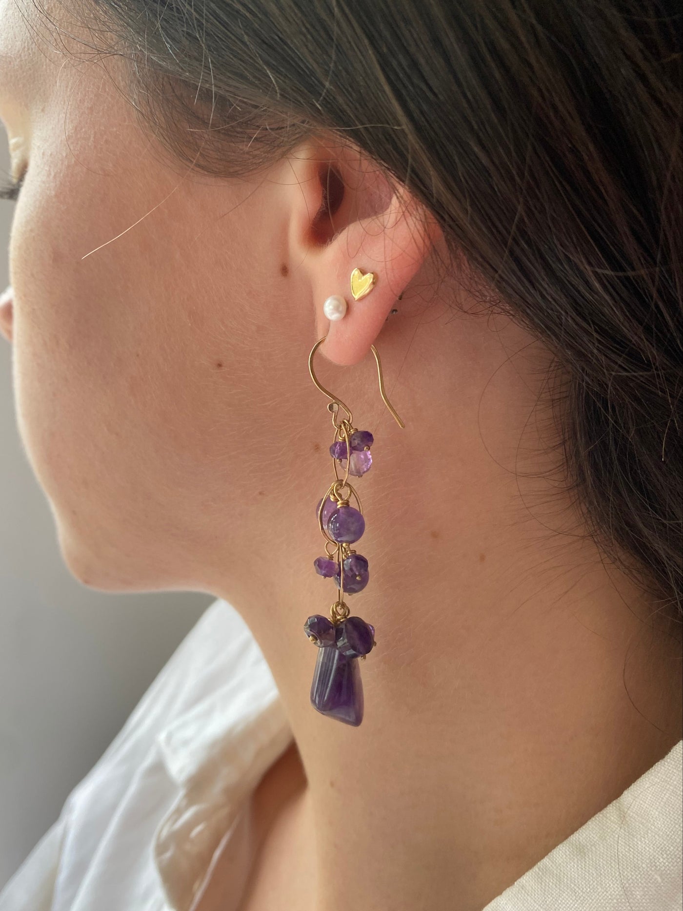 Close-up of an ear with a gold earring featuring purple gemstones.