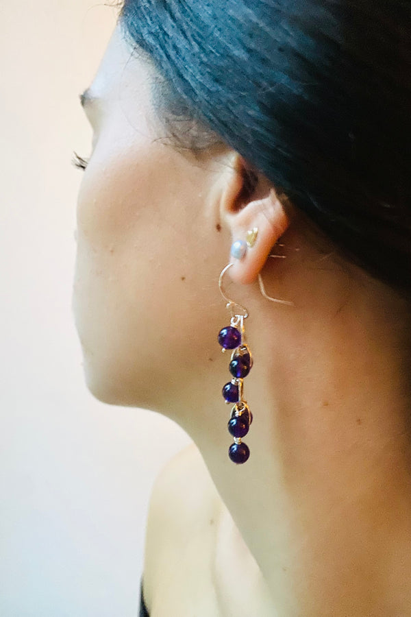 Close-up of a waterfall earring with purple  amethyst gemstone beads worn by a model against a plain background.