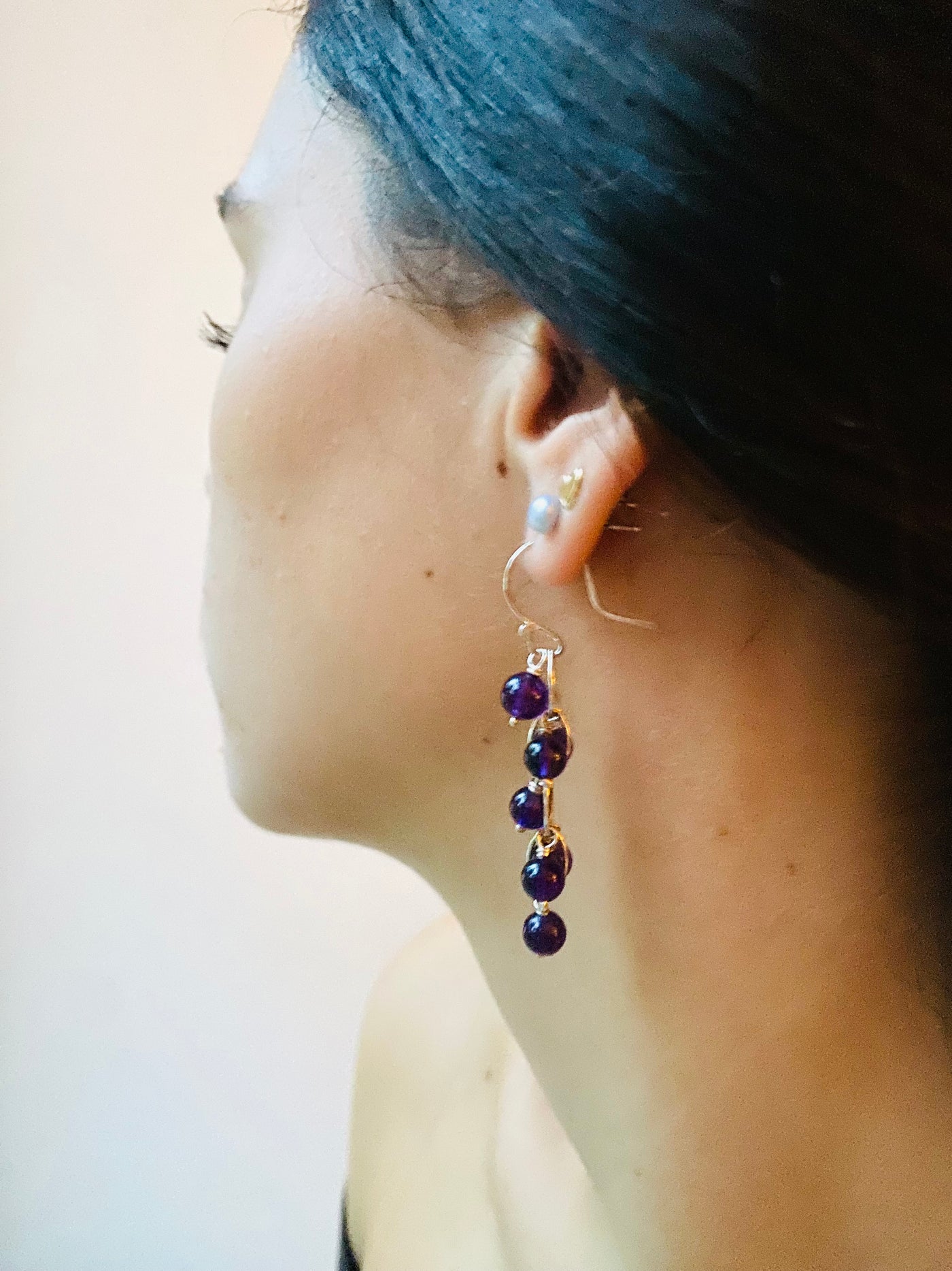 Close-up of a waterfall earring with purple  amethyst gemstone beads worn by a model against a plain background.
