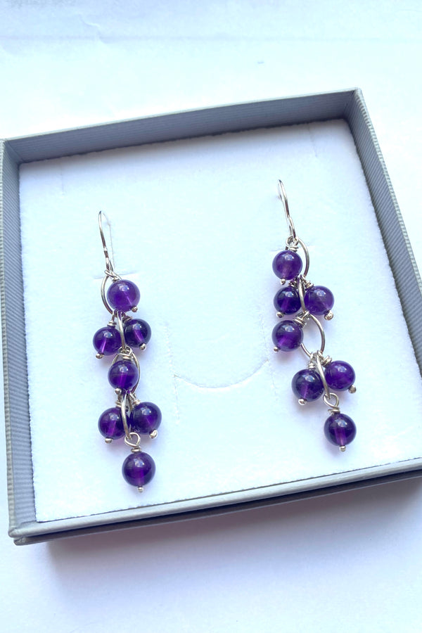 Pair of purple beaded amethyst earrings in a gray gift box on a white background