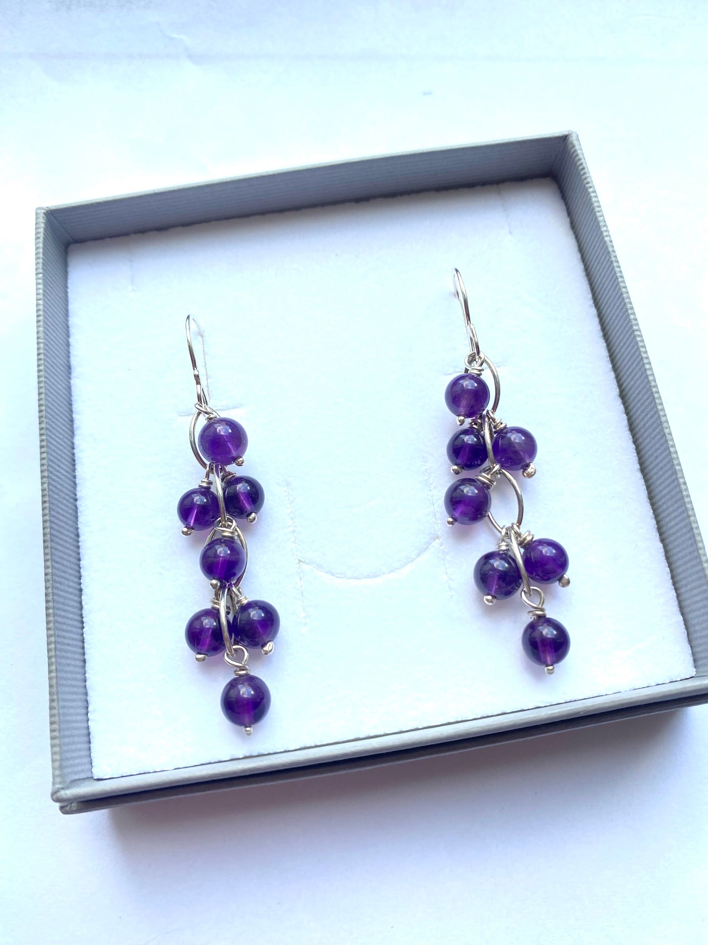 Pair of purple beaded amethyst earrings in a gray gift box on a white background