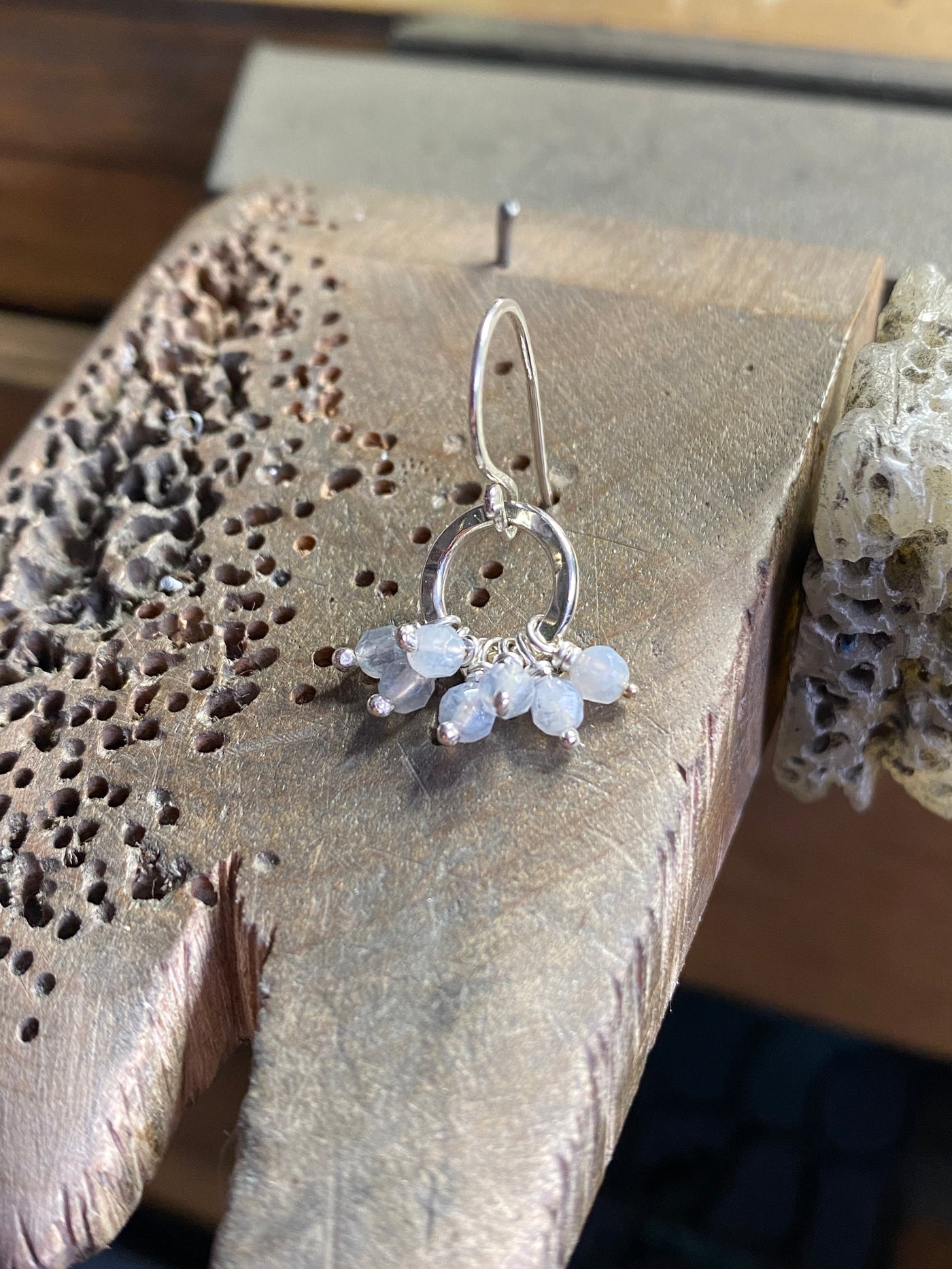 Silver earring with small stones on a textured jewellers bench peg