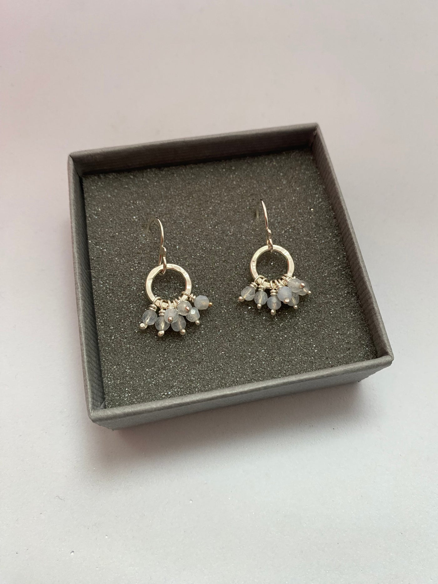 Pair of silver earrings with gemstones in a gray box on a light gray background