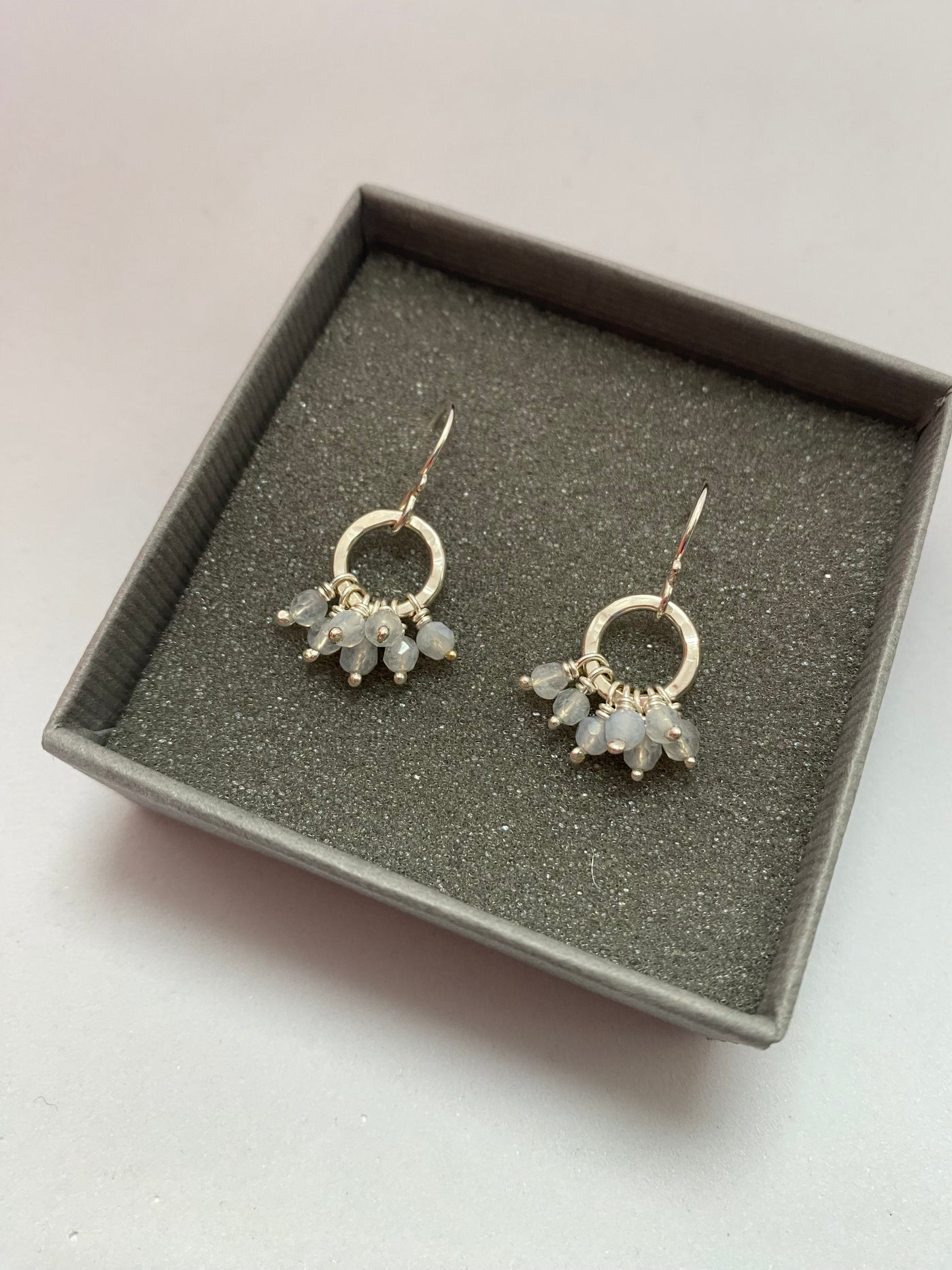 Pair of gemstone earrings in a gray jewelry box on a light background