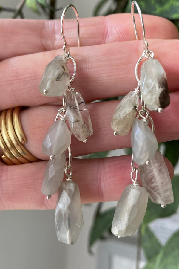 Beautiful waterfall earrings handmade in sterling silver, with luminous moonstone beads hanging from silver links. Displayed on the hand that made them. 
