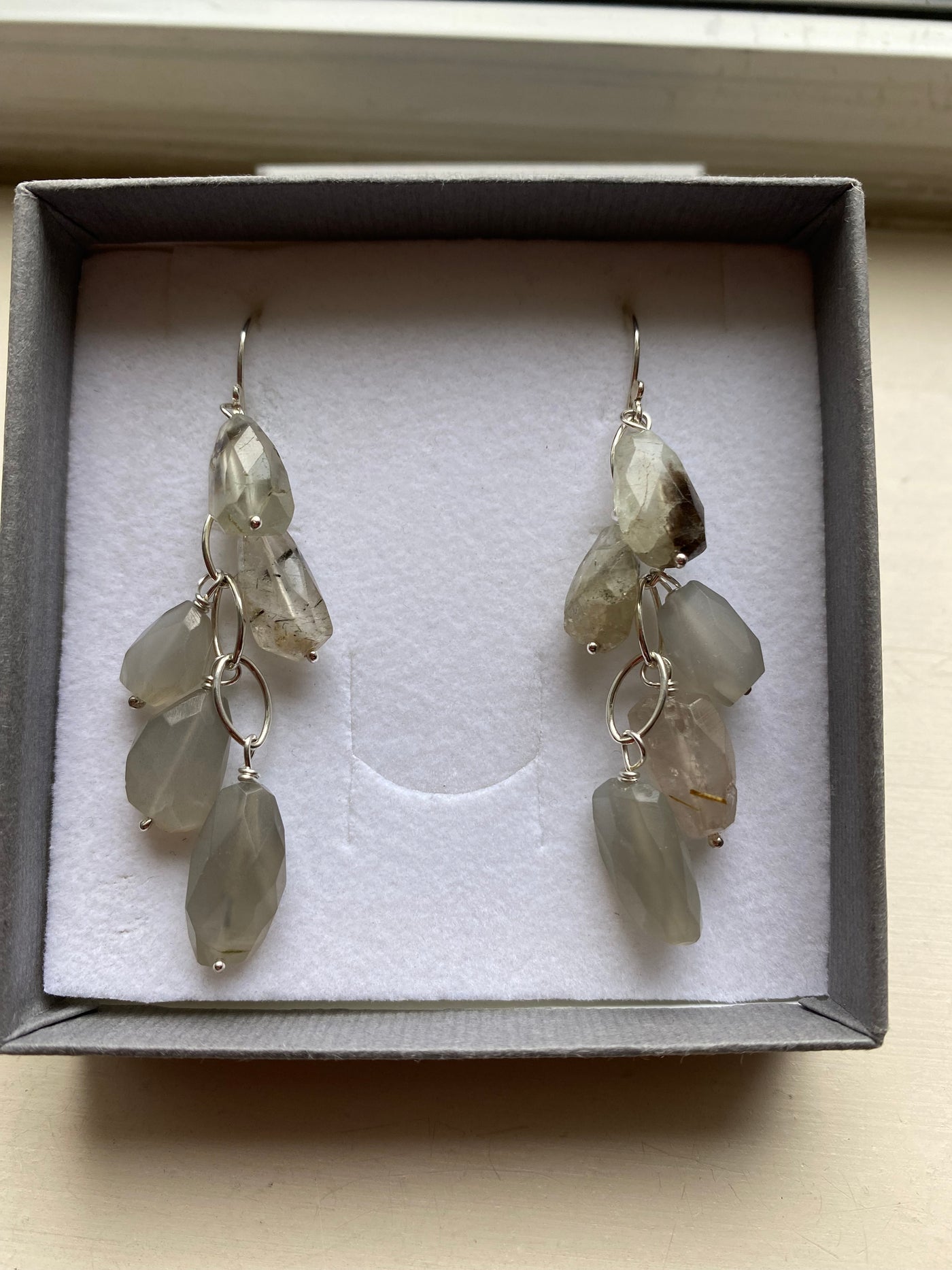 Pair of earrings with grey moonstone gemstones stones in a box on a beige surface