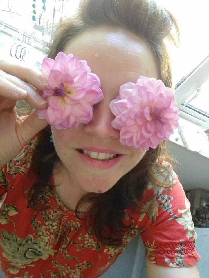 Athene Sholl holding pink flowers over her eyes. 