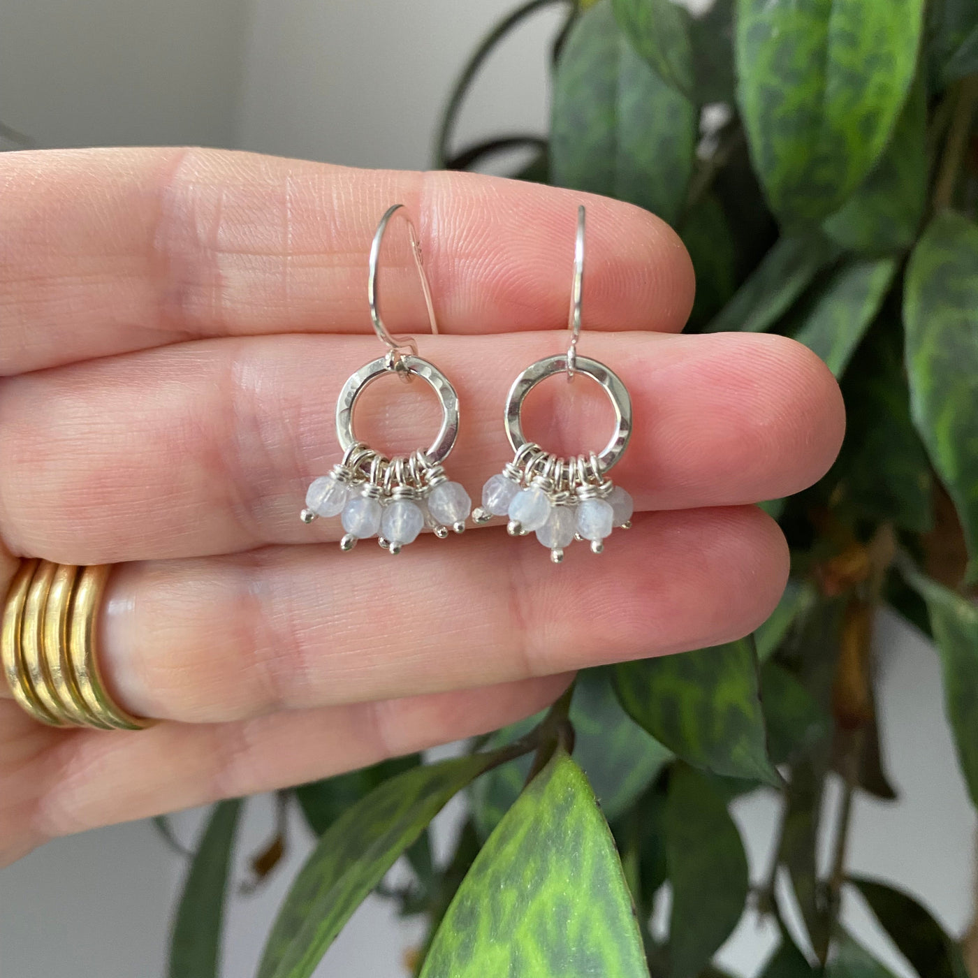 Silver earrings with small aquamarine stones held between fingers against a green leafy background