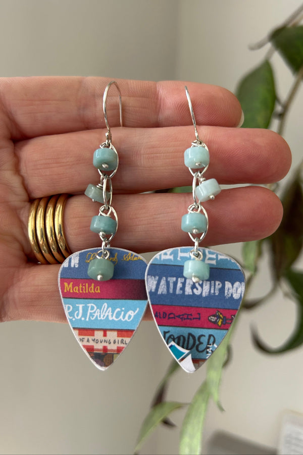 Dangly earrings made from recycled plastic book token cards, displayed on the hand that made them