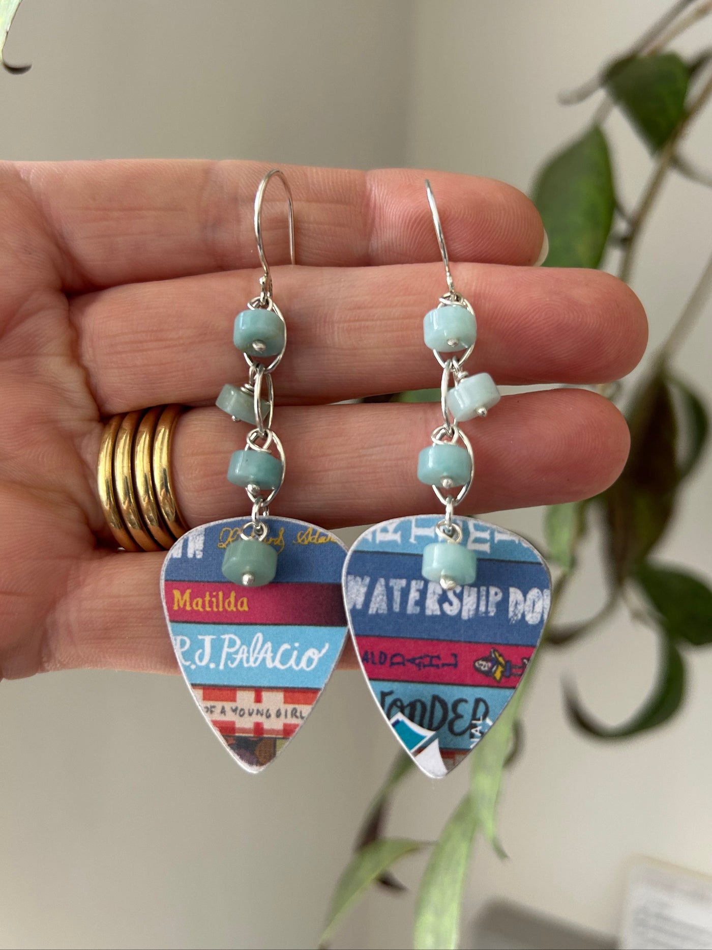 Dangly earrings made from recycled plastic book token cards, displayed on the hand that made them