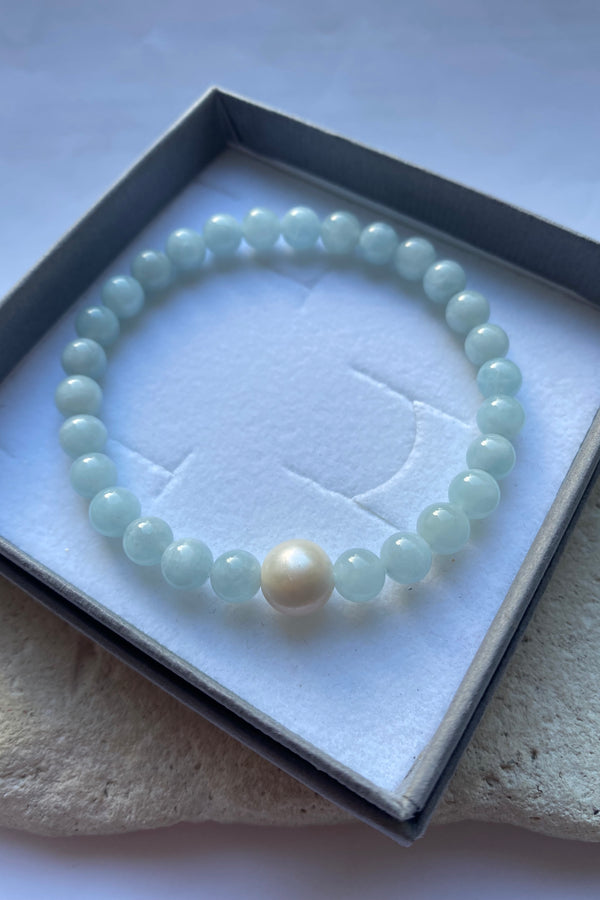 aquamarine bead bracelet with a single larger pearl on a white background inside a grey gift box.