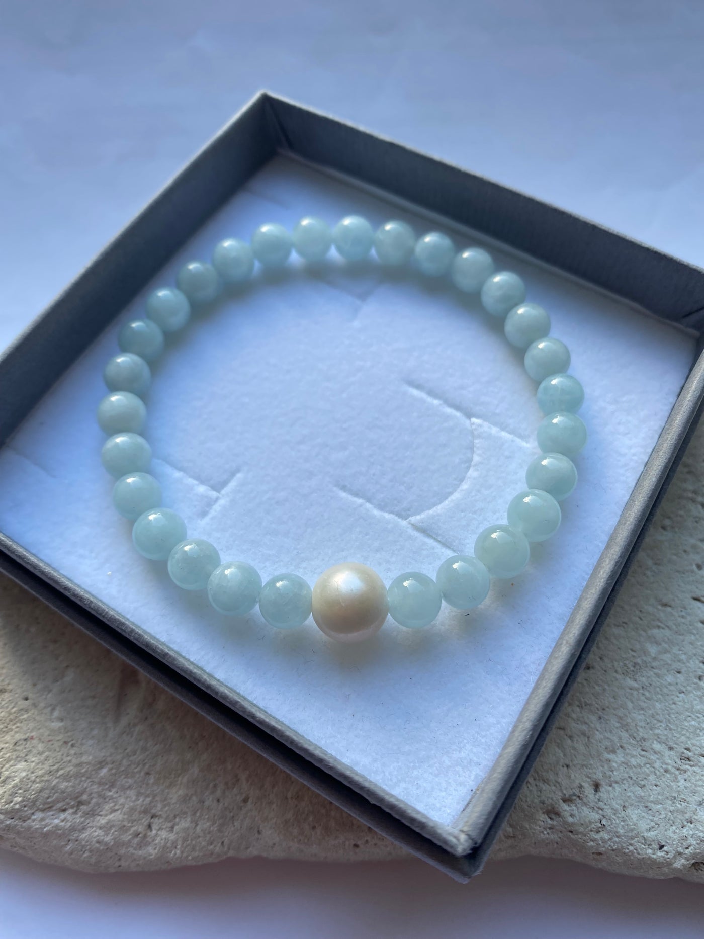 aquamarine bead bracelet with a single larger pearl on a white background inside a grey gift box.