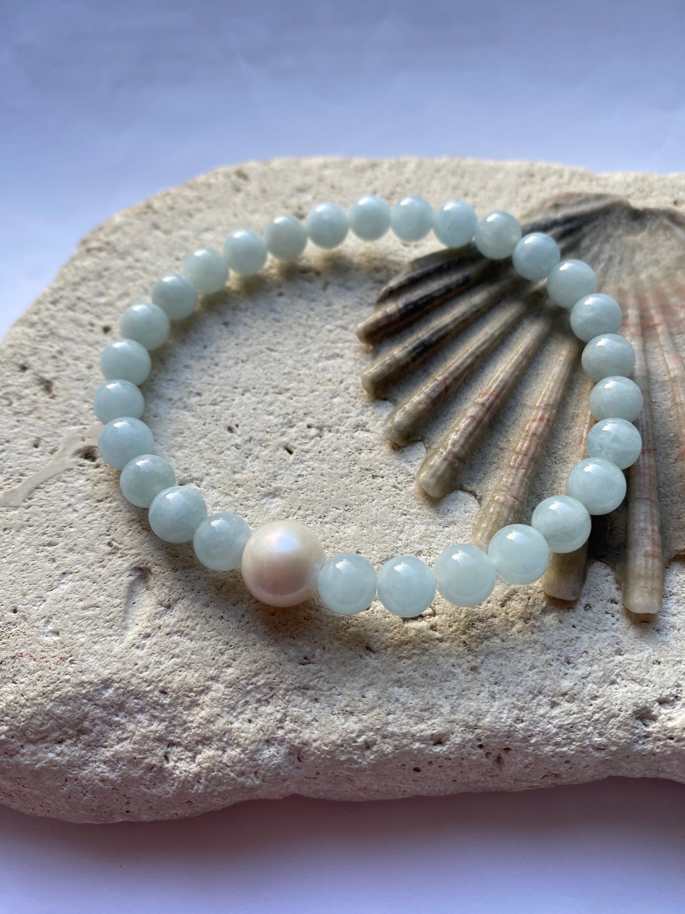 Pearl and aquamarine gemstone bracelet on a stone surface with a shell