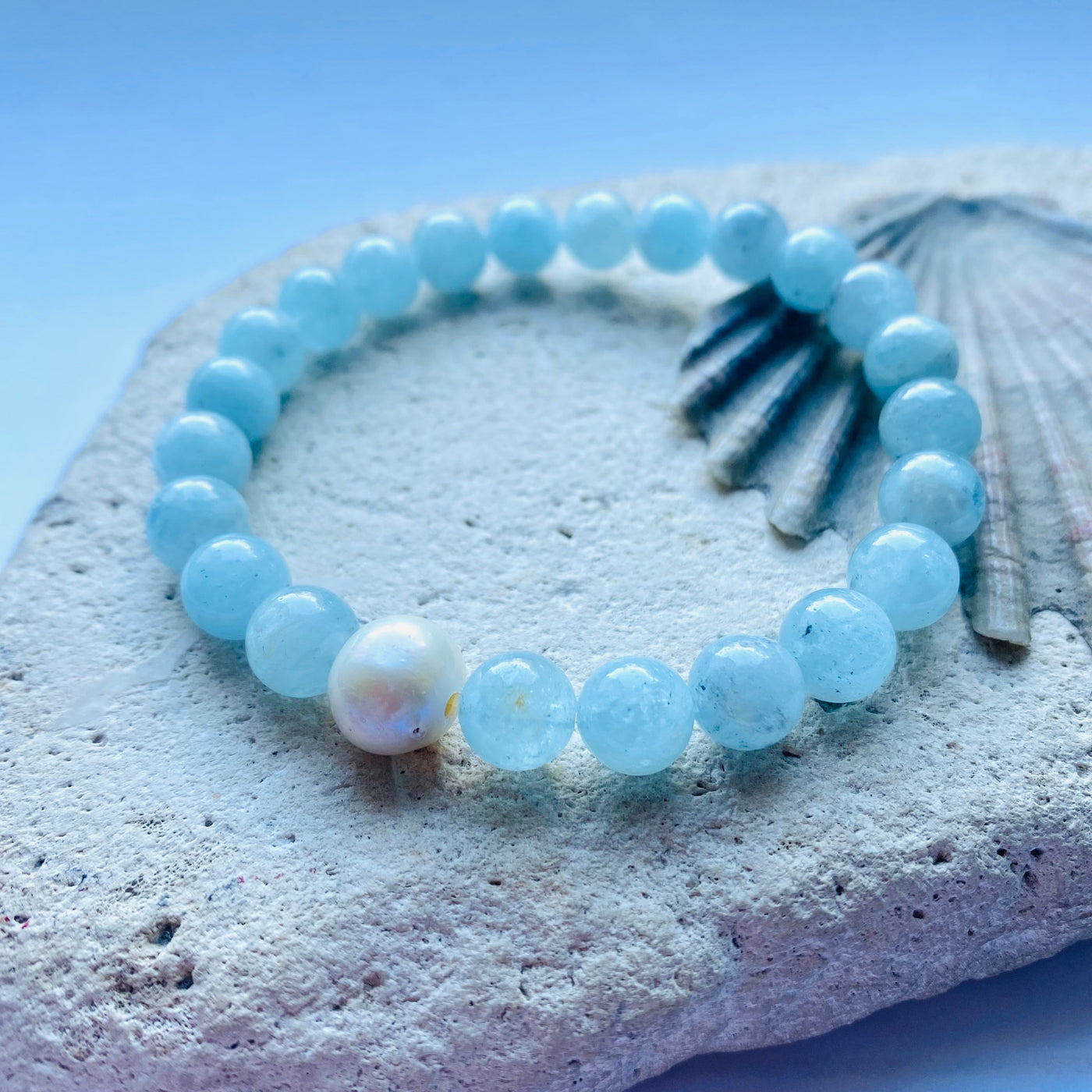 Pale blue beaded aquamarine gemstone bracelet with a freshwater pearl accent on a rock and shell background