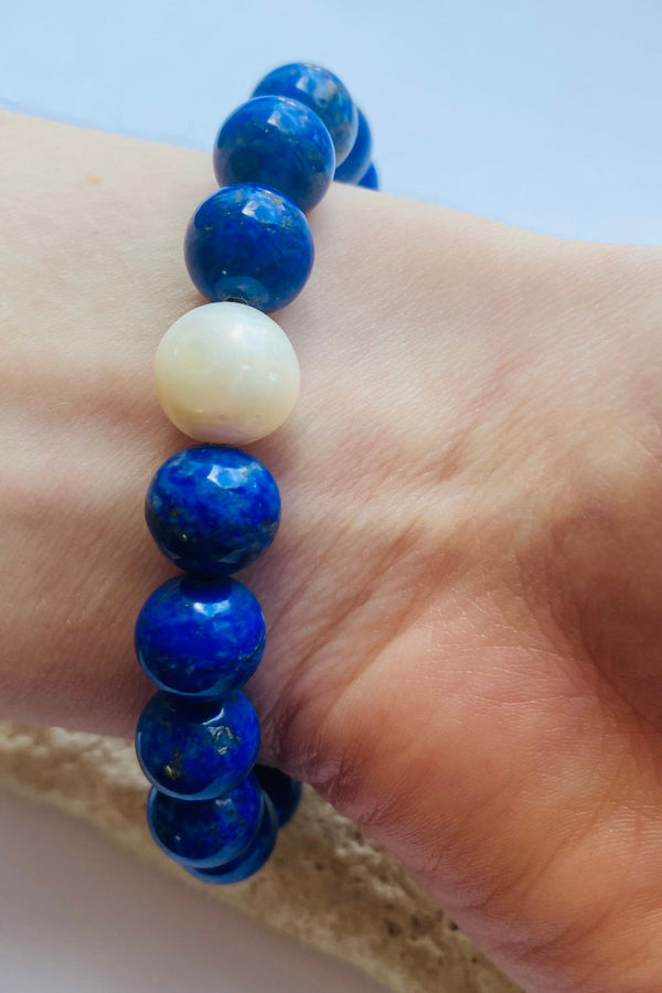 Blue beaded lapis lazuli bracelet with a freshwater pearl saccent worn on a wrist with a light background