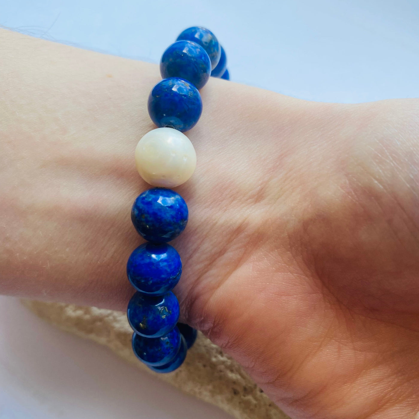 Blue beaded lapis lazuli bracelet with a freshwater pearl saccent worn on a wrist with a light background