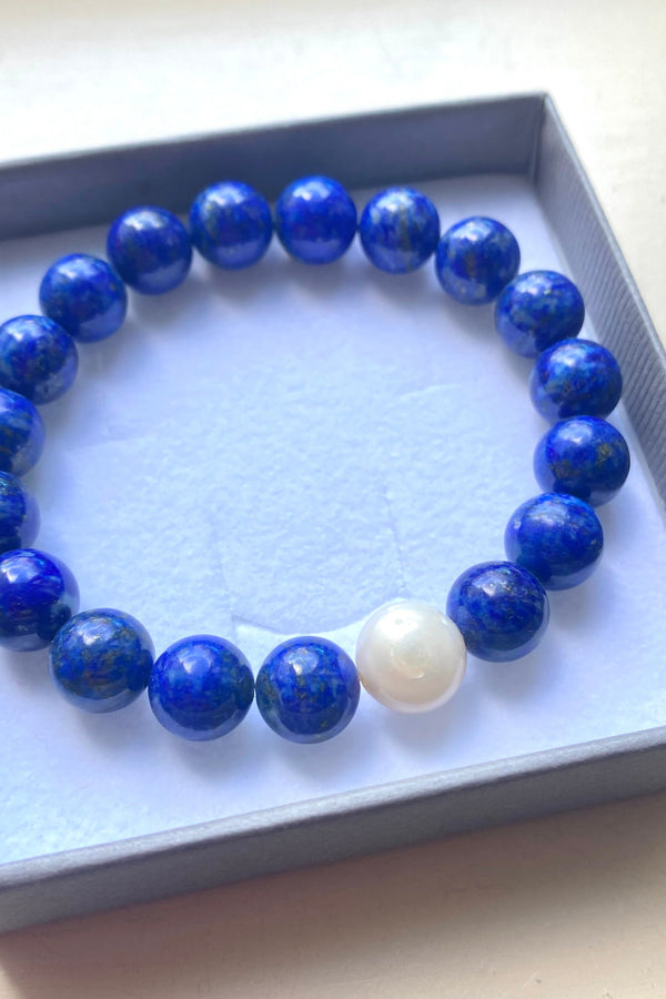 Blue beaded lapis lazuli bracelet with a white pearl in a gift box on a light background
