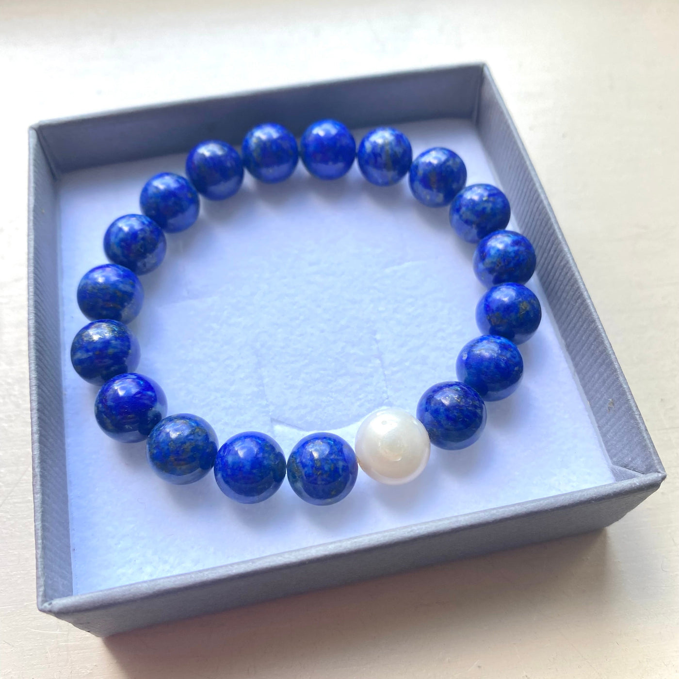 Blue beaded lapis lazuli bracelet with a white pearl in a gift box on a light background