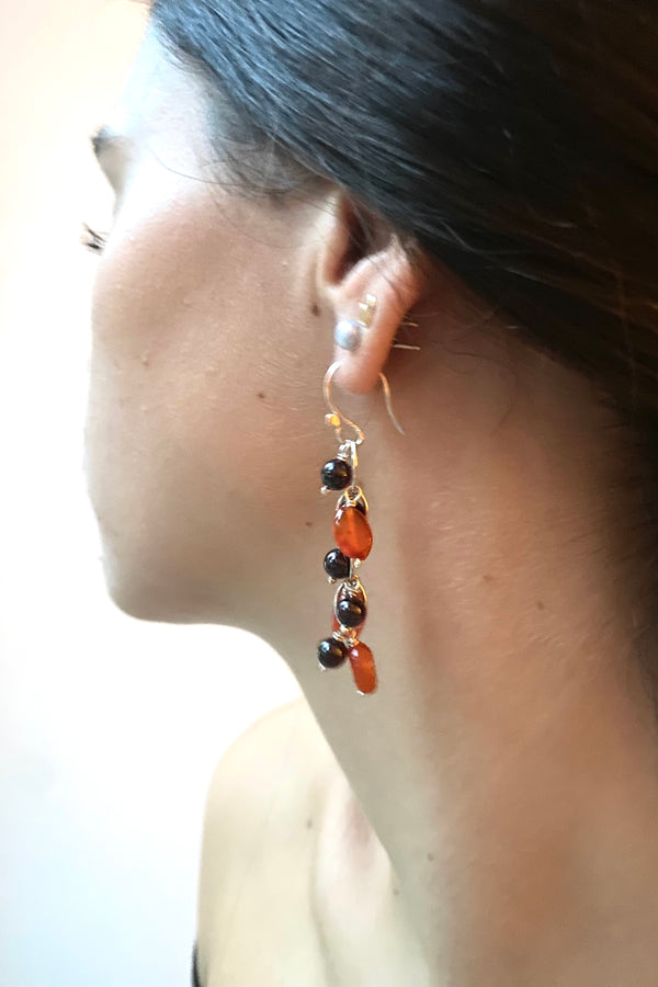 Close-up of a waterfall earring with carnelian and garnet gemstone beads worn by a model against a plain background. 