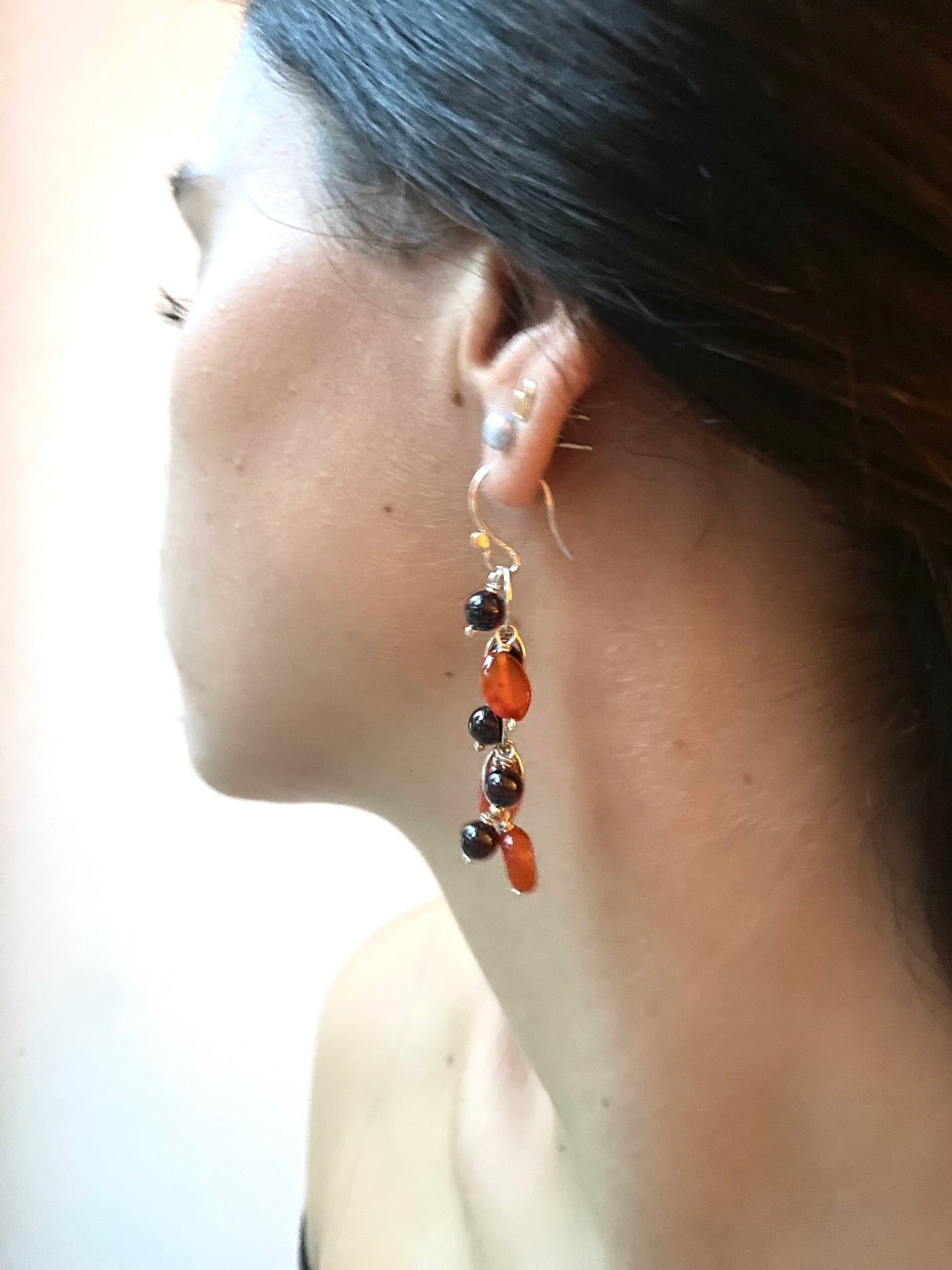 Close-up of a waterfall earring with carnelian and garnet gemstone beads worn by a model against a plain background. 