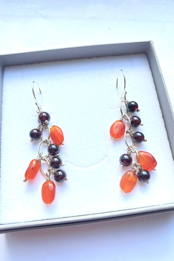 Pair of earrings with vivid orange carnelian and deep red garnet polished gemstone  beads in a gift box on a white background