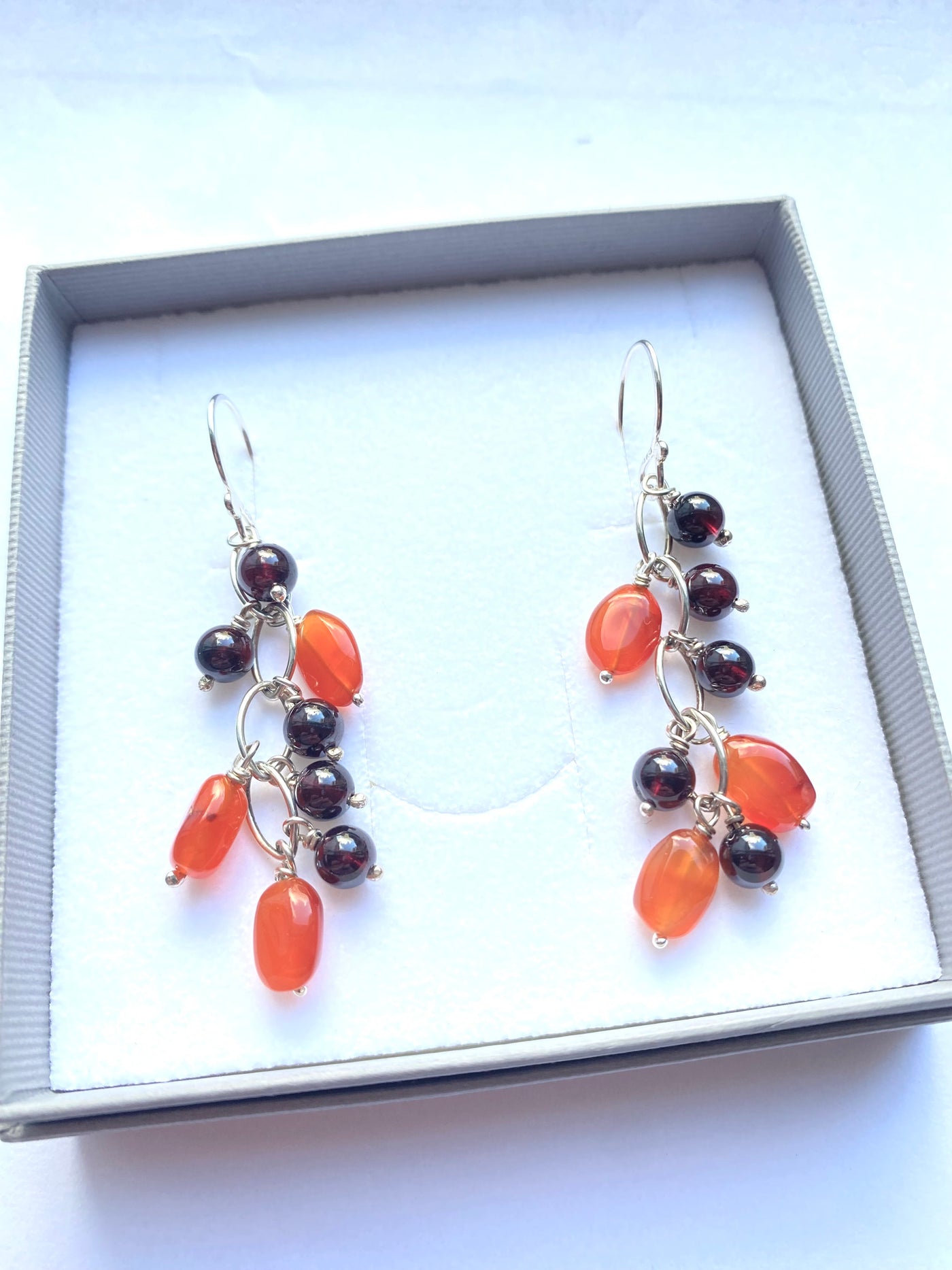 Pair of earrings with vivid orange carnelian and deep red garnet polished gemstone  beads in a gift box on a white background