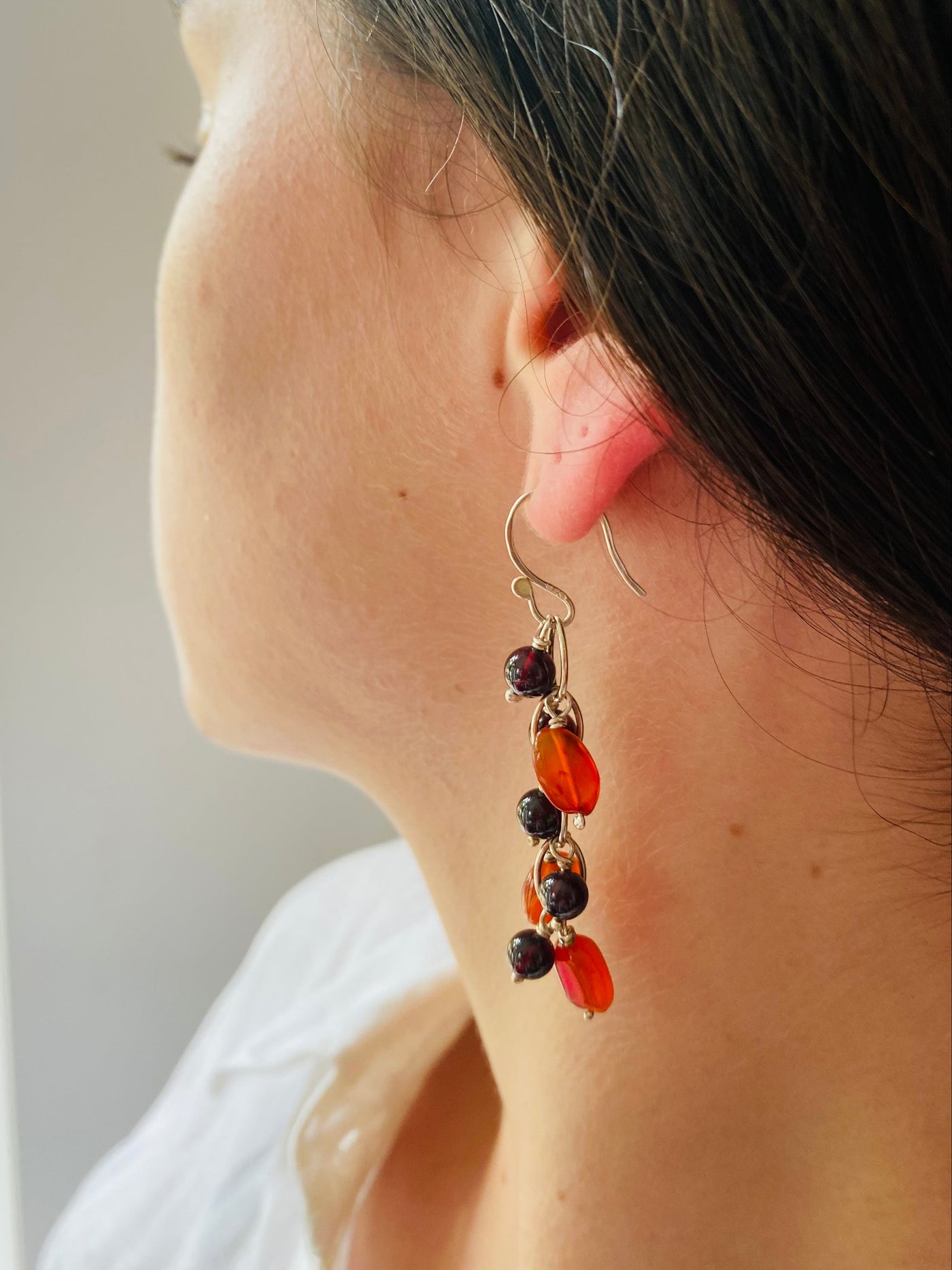 Close-up of a waterfall earring with carnelian and garnet gemstone beads worn by a model wearing a white blouse.