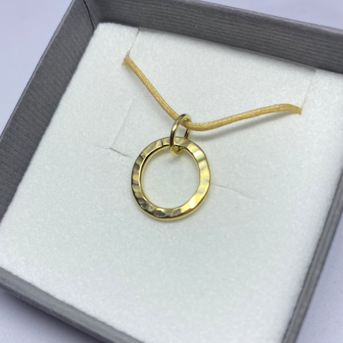 Circular textured yellow gold polished pendant in a gray gift box on a white background