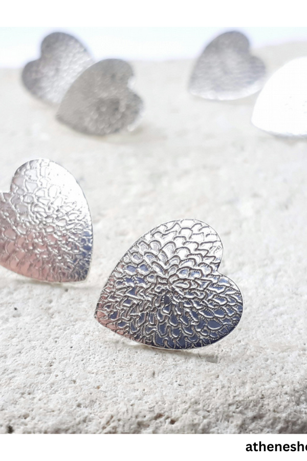 Silver heart-shaped earrings on a textured white surface with 'athenesholl.com' branding.
