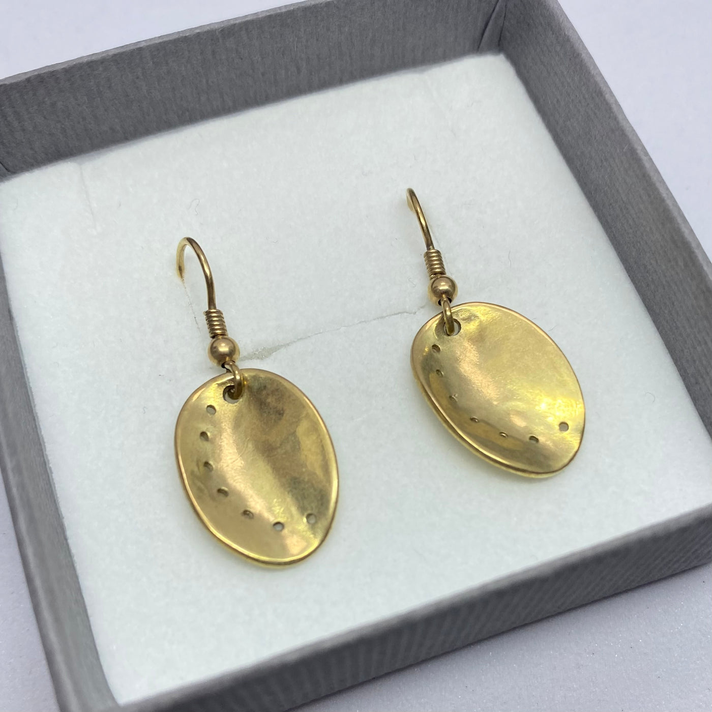 Gold earrings in a gray box on a white background. 