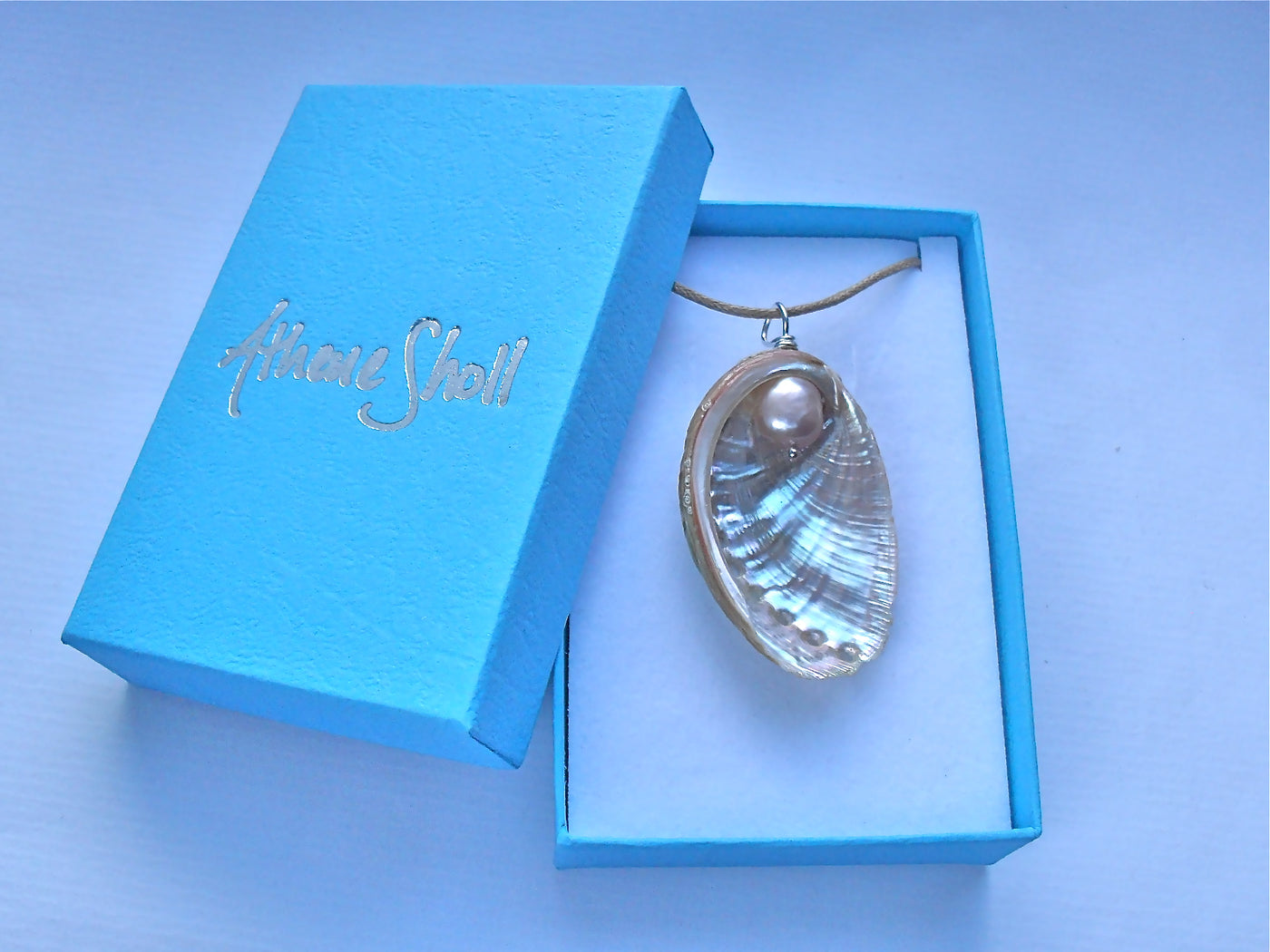 Shell pendant necklace in a blue box with 'Athene Sholl' branding.