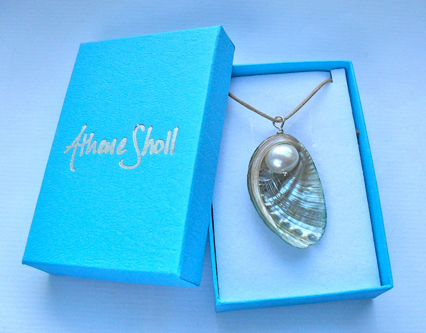 Shell pendant necklace in a blue box with 'Athene Sholl' branding.