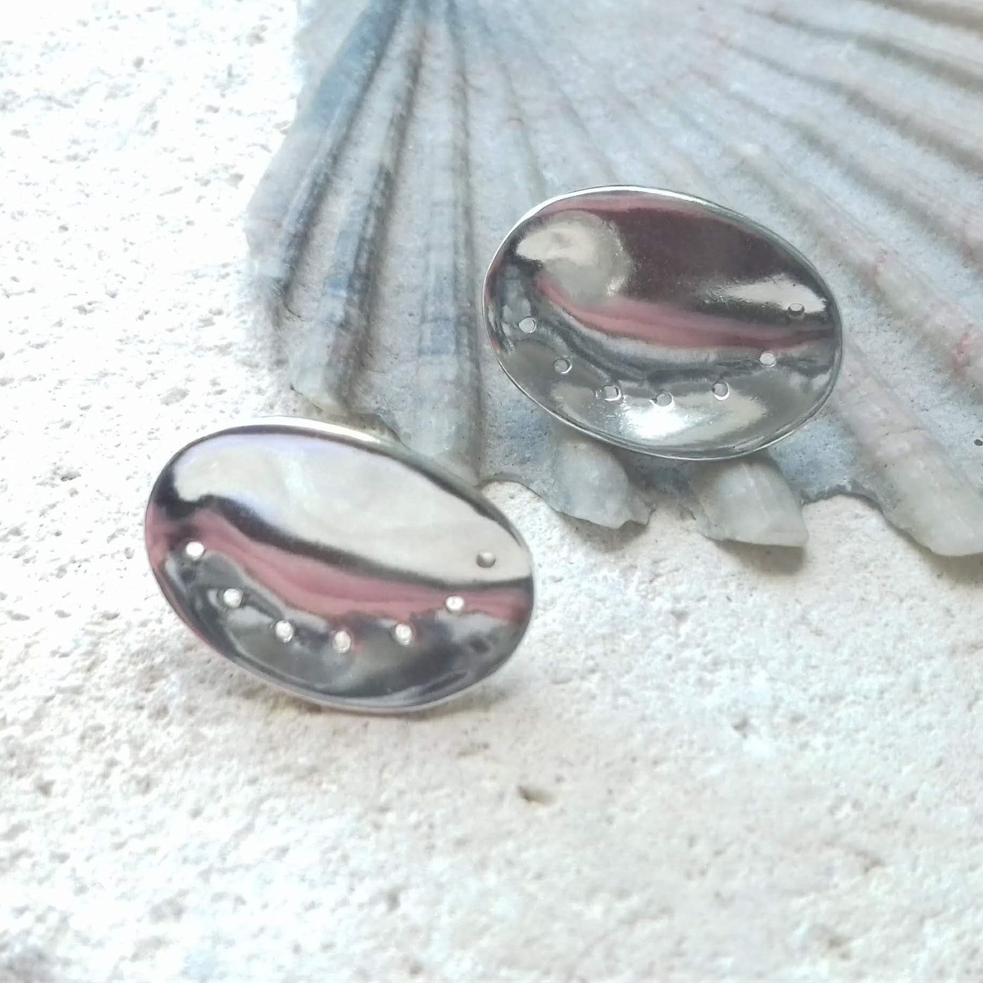 Highly polished silver guernsey ormer earrings on a shell background