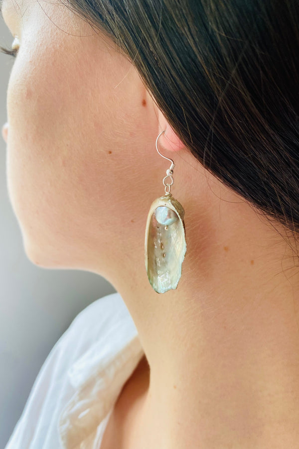 Close-up of a Guernsey ormer shell earring worn on a model, earrings has a grey freshwater pearl and an irridescent surface. 