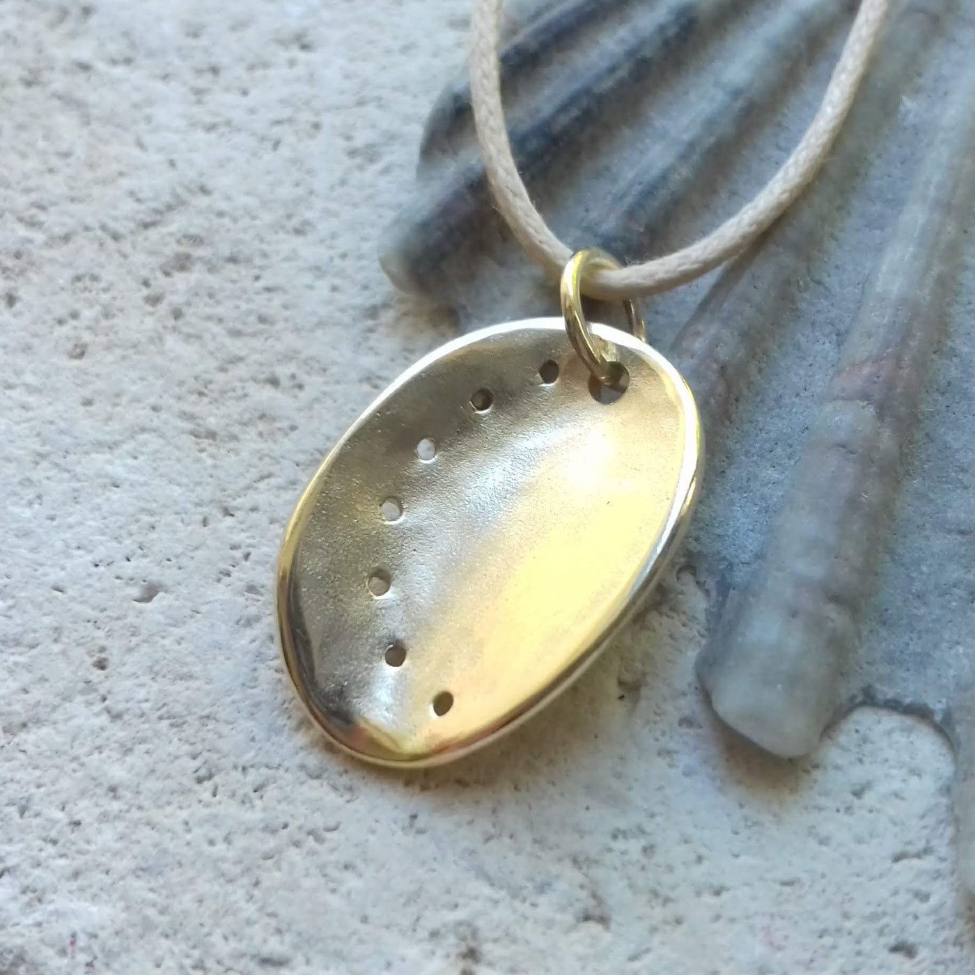 Guernsey ormer shell pendant in 9ct yellow gold on a cotton cord, laid on a seashell background