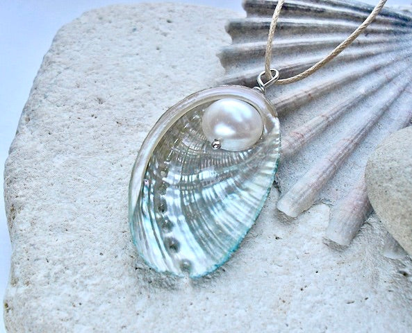 Shell pendant with a white pearl on a stone surface