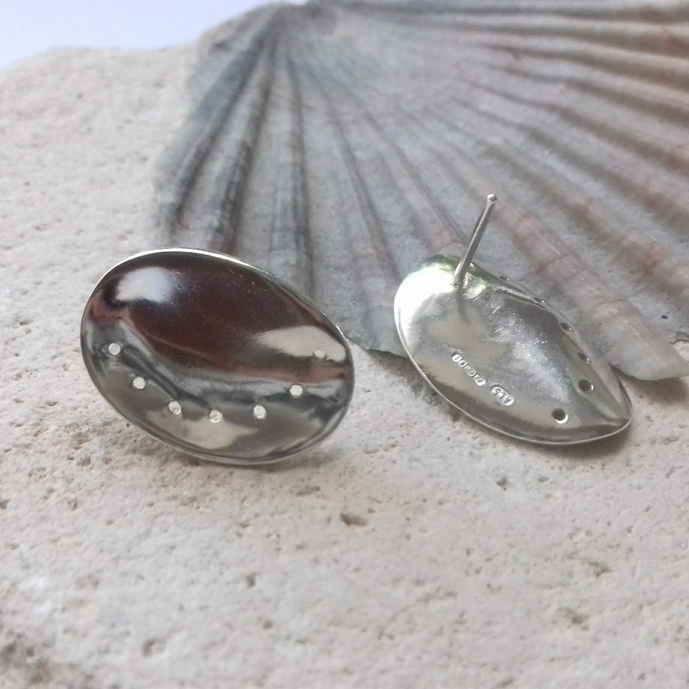 Polished silver ormer earrings on a shell background. Hallmark from the London Assay Office is visible. 