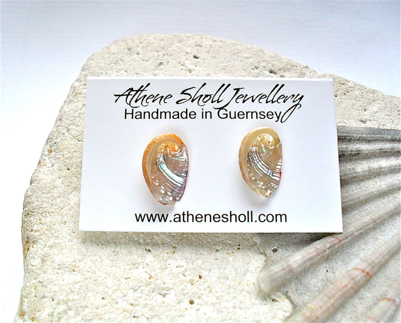 Shell earrings on a card with 'Athenе Shоll Jewellerу' branding, displayed on a rock.